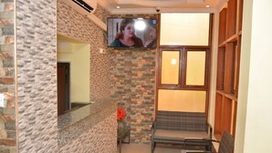 Un área de recepción con pared de piedra, un televisor de pantalla plana sobre el mostrador y una zona de estar con sillas de mimbre.