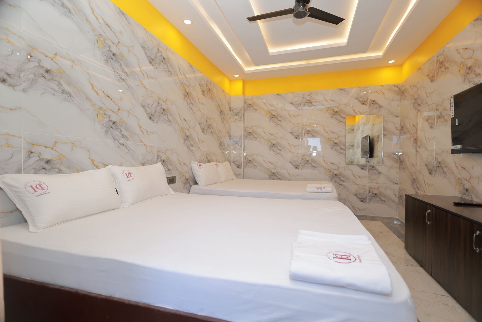 Una habitación de hotel con una cama grande, una mesita de noche, un espejo y un ventilador de techo.