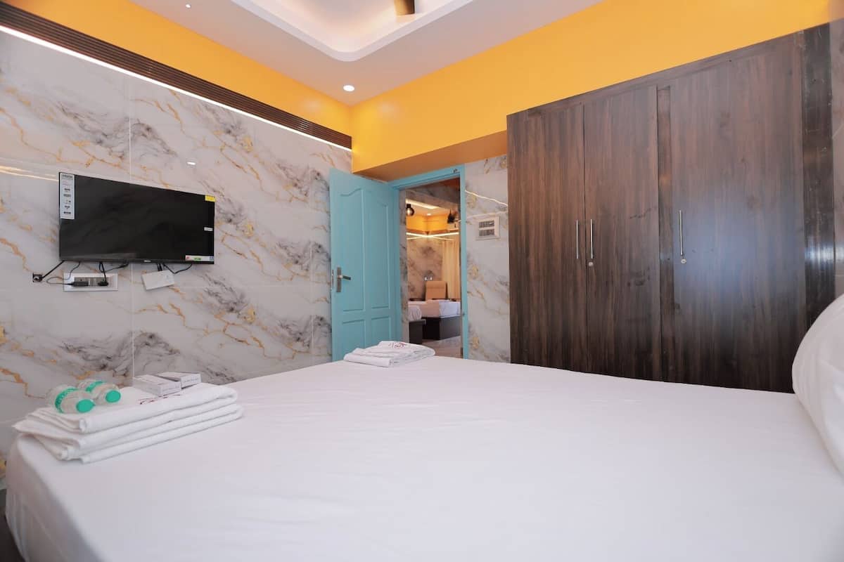 A hotel room with a bed, a TV mounted on the wall, a wardrobe, and a bathroom visible through an open door.