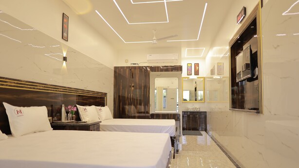 Quarto de hotel com duas camas, uma toucador com espelho, uma televisão presa na parede e teto com iluminação geométrica.