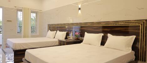 Habitación de hotel con dos camas, una pared de mármol, un ventilador de techo y una mesita de noche con un jarrón de flores.