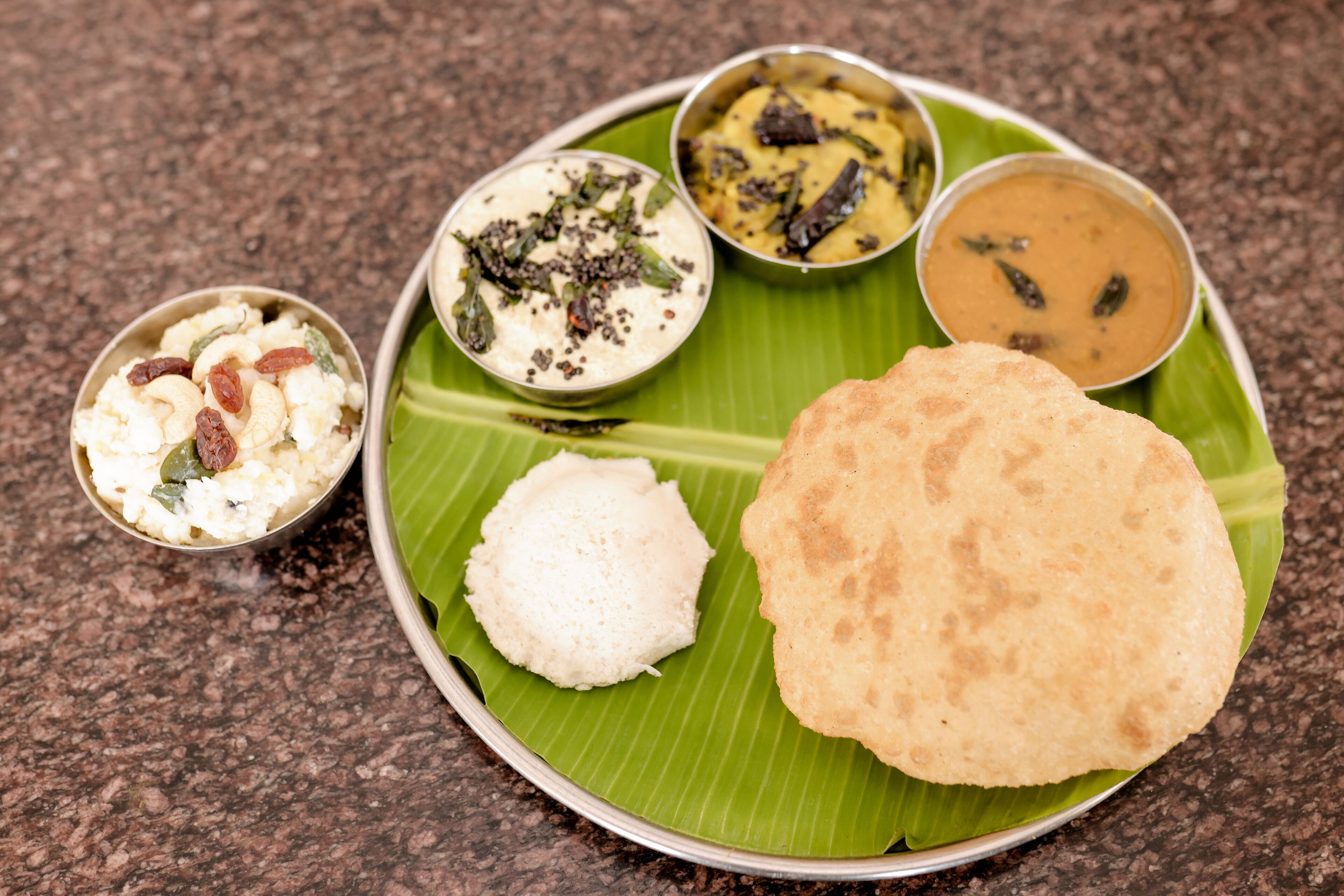 A traditional South Indian meal served on a banana leaf with rice, a flatbread, and three types of sambar.