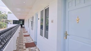 Um corredor com piso xadrez, uma porta azul com puxador dourado e uma varanda com corrimão.