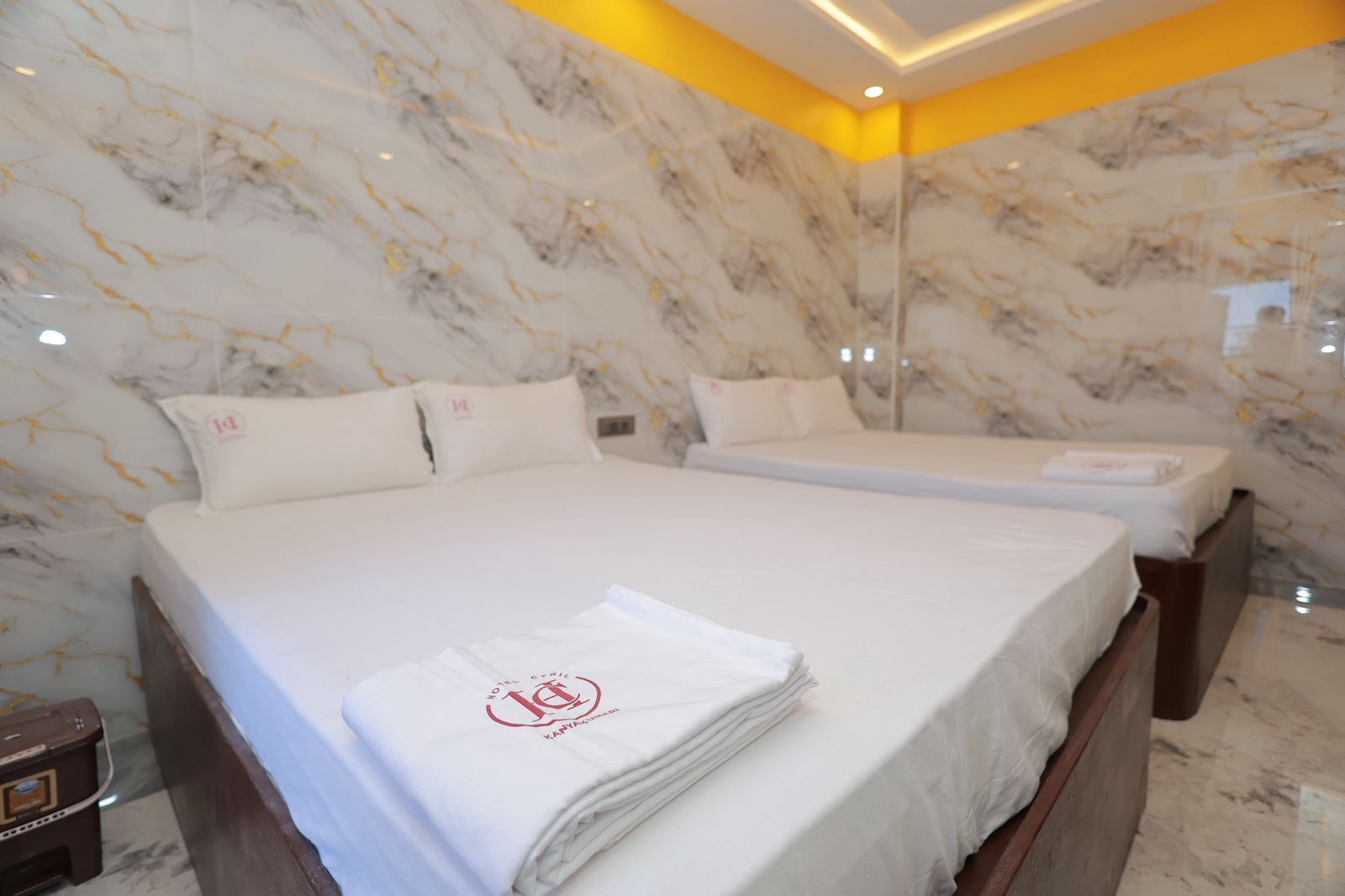Une chambre d’hôtel avec deux lits, des murs en marbre et un mur d’accent jaune.