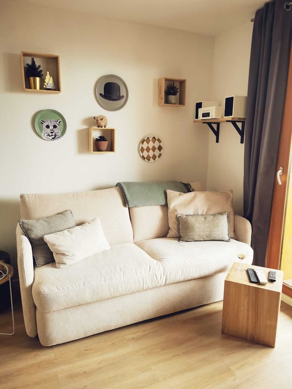 A living room with a beige sofa, a small wooden side table, and various wall decorations including a leopard plate, a hat, and a shelf with a speaker.