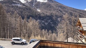 A mountain cabin with a wooden exterior, a balcony, and a view of snow-capped mountains.