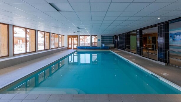 An indoor swimming pool with clear glass walls, a tiled floor, and a ceiling with recessed lighting.