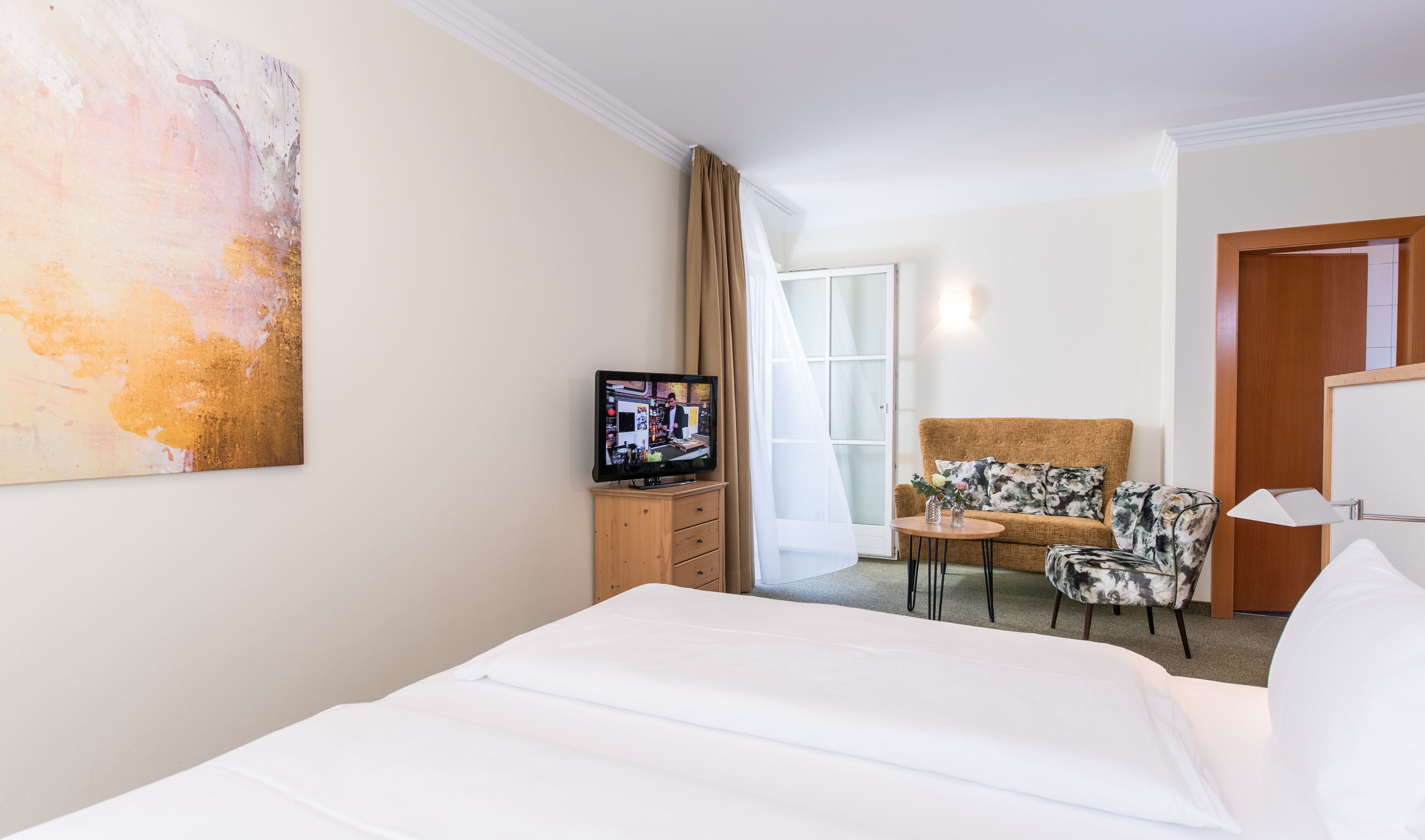 A hotel room with a bed, a television, a sofa, a chair, and a painting on the wall.