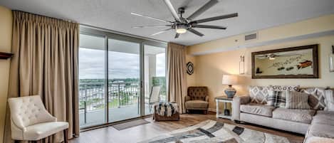A spacious living room with a large window, a ceiling fan, a sofa, a chair, and a rug.