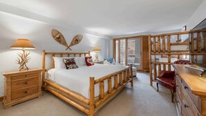 A spacious bedroom with a large bed, wooden headboard, bedside tables, a dresser, and a sliding glass door leading to a balcony.