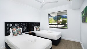 A hotel room with two beds, a ceiling fan, a window with a view of the outdoors, and a decorative wall panel.