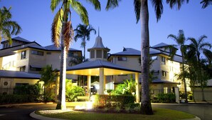 A hotel with a covered entrance, palm trees, and a well-maintained lawn.
