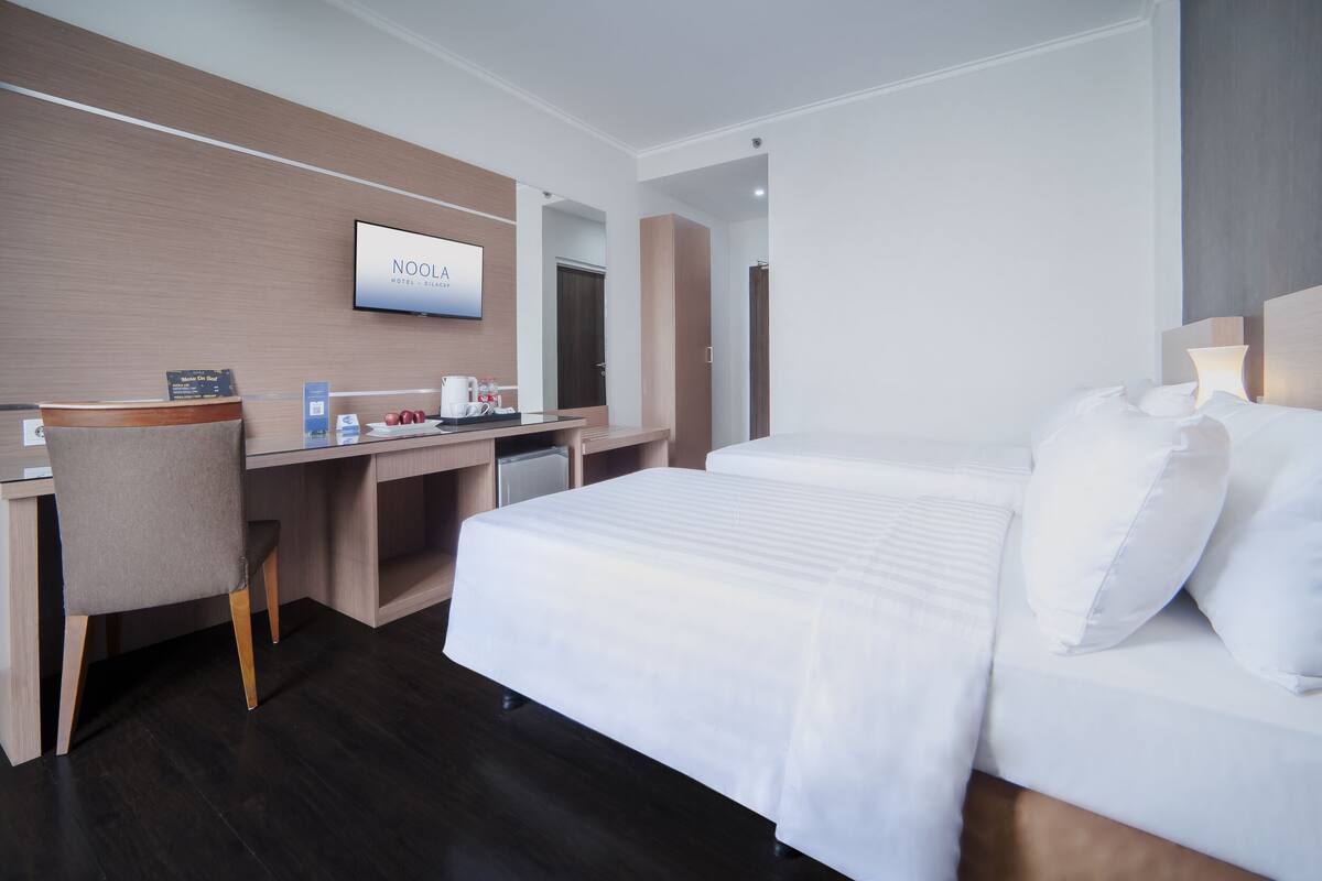 A hotel room with a bed, a desk, a chair, a TV, and a mirror.