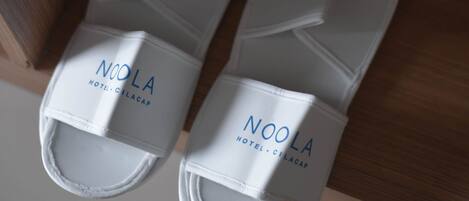 A pair of white Noolia slippers with the hotel name visible on the strap.