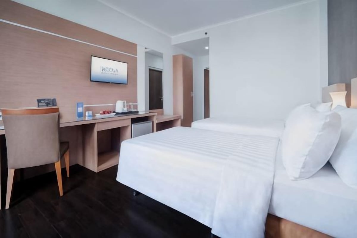 A hotel room with a bed, a desk, a chair, a TV, and a mirror.