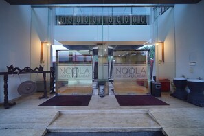 La entrada del Hotel NoDLA con puertas de vidrio, piso de mármol y una alfombra roja que conduce a la entrada.