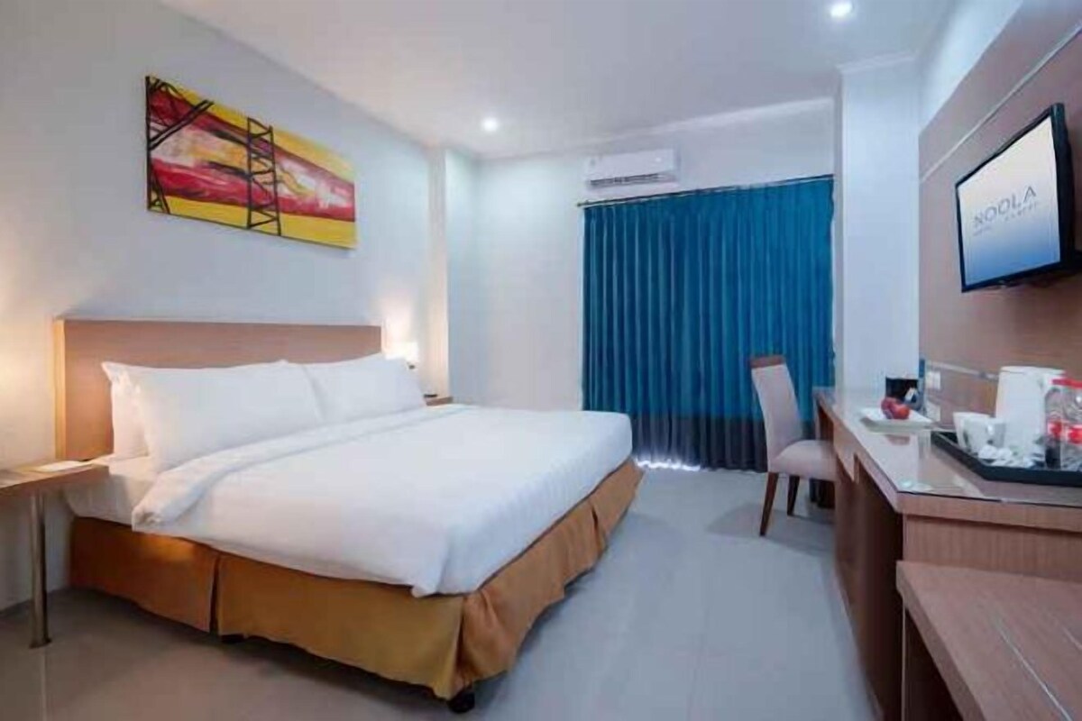 A hotel room with a bed, a desk, a chair, and a TV on the wall.