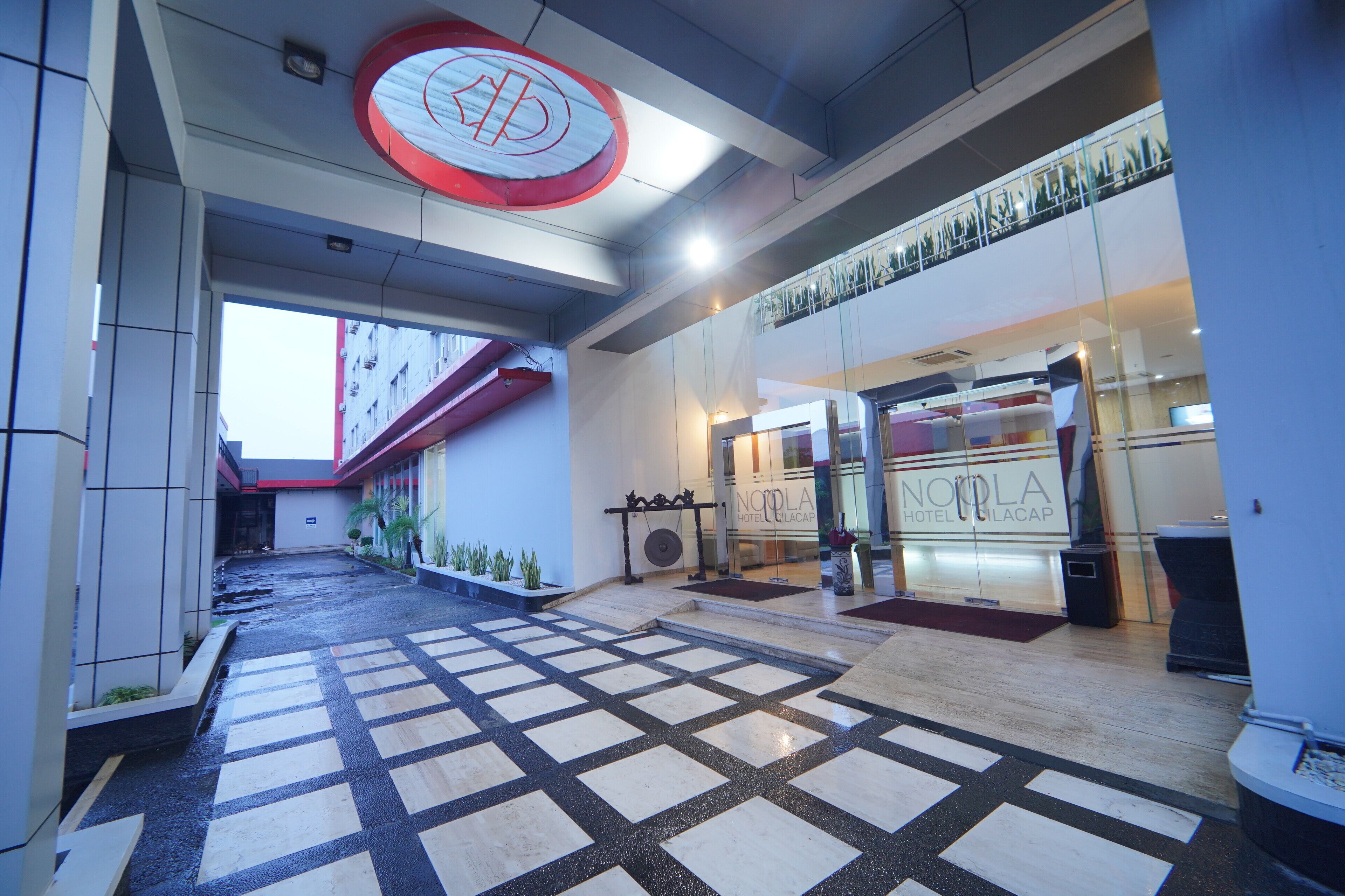A hotel lobby with a checkered floor, a large circular sign with a logo, and a glass entrance to the hotel.