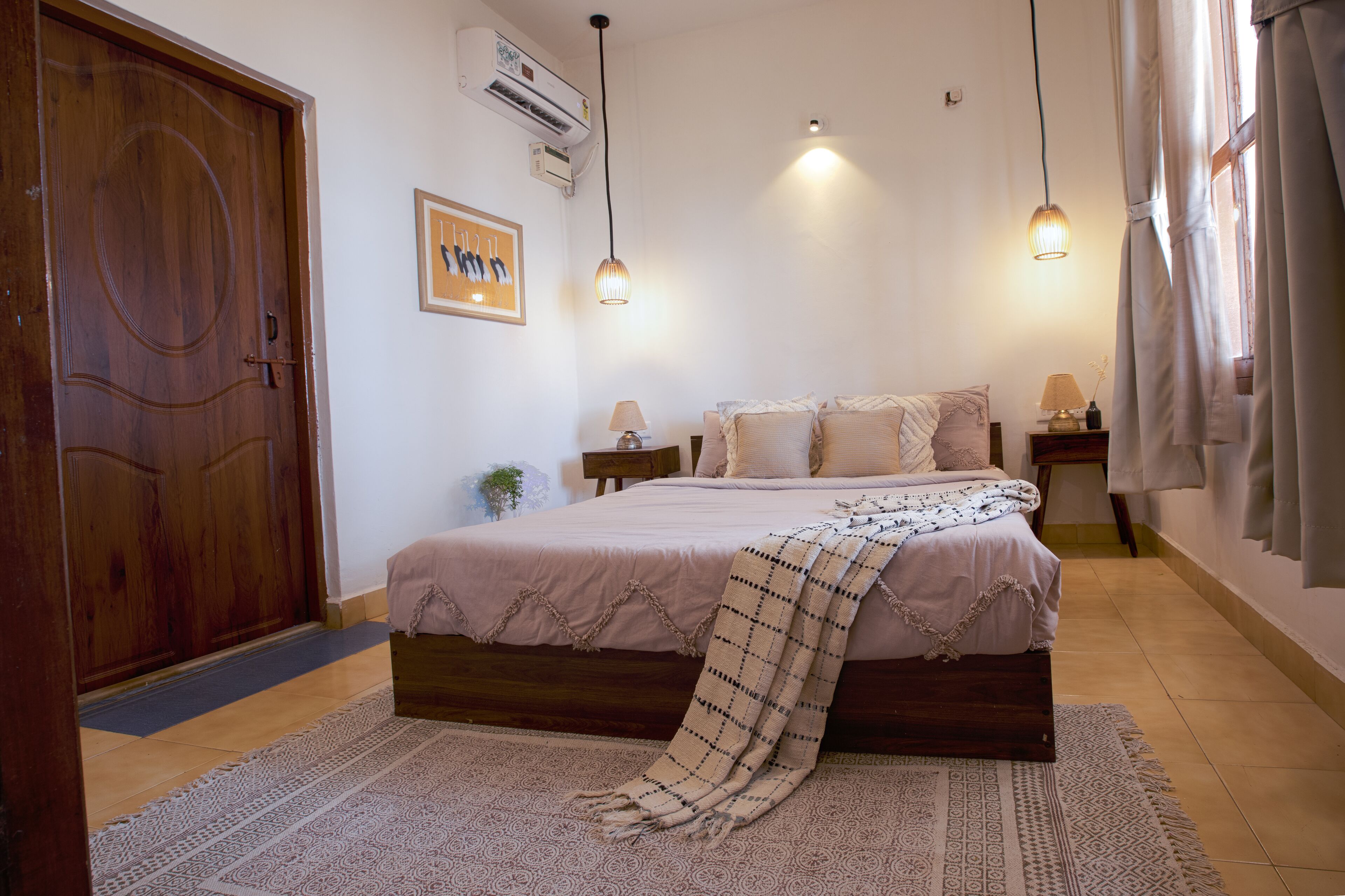 Een slaapkamer met een houten deur, een bed met een geborduurd plaid, twee bedlampen en een luchtverwarmer aan de muur.