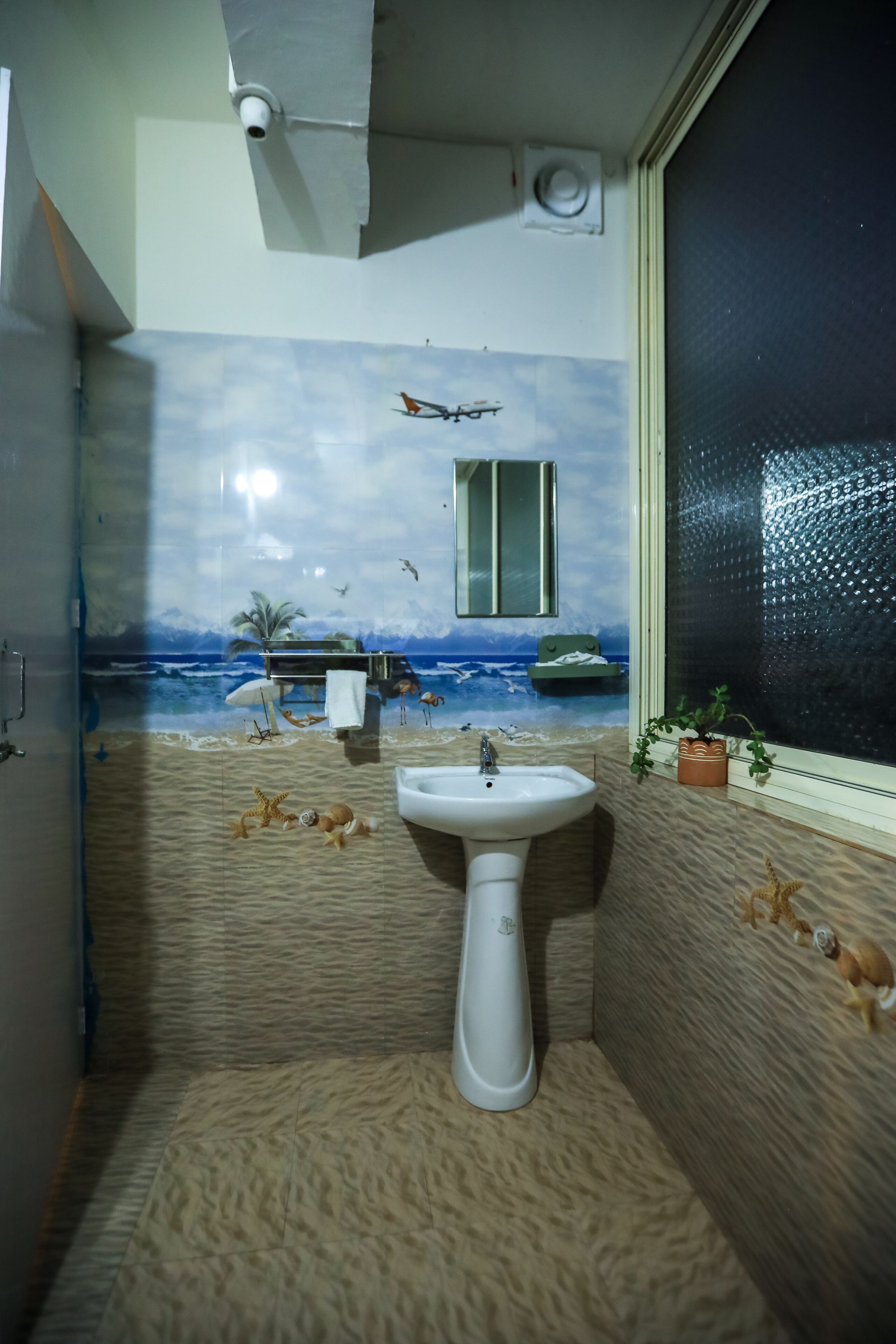 A bathroom with a beach mural, a sink, and a window with a view.