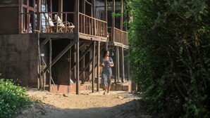 A wooden building with a balcony, a chair, and a person walking. - Woodpegger By The Beach (Mandrem)