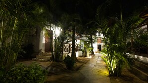 A nighttime outdoor pathway with stone steps leading to a building, surrounded by palm trees and illuminated by ambient lighting. - Woodpegger By The Beach (Mandrem)
