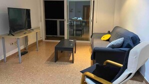 Un saló amb un sofà, una taula de centre, una televisió sobre un suport i una porta corredissa de vidre que dona a un balcó.