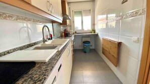 Cuina estreta amb armaris blancs, taulell de granat i una finestra que aporta llum natural.