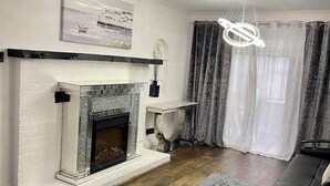 Un salon moderne avec une cheminée, une œuvre d’art accrochée au mur, un luminaire contemporain et un tapis gris.