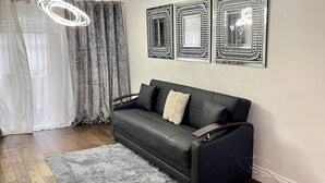 Un salon moderne avec un canapé en cuir noir, un tapis moelleux de couleur grise et trois miroirs décoratifs fixés au mur.