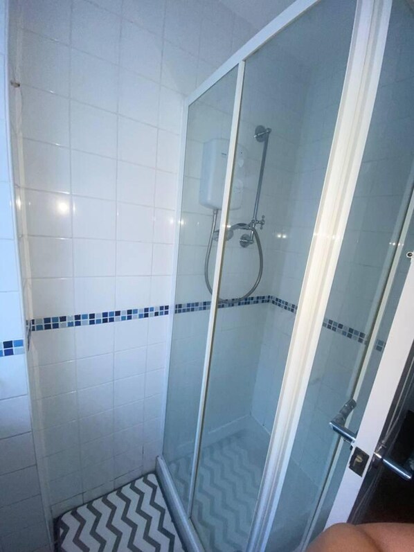 A glass-enclosed shower with a white tiled wall and a blue tile border.