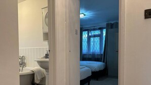 Une chambre avec un lit simple, une fenêtre avec des rideaux et une salle de bain avec une baignoire et un lavabo.