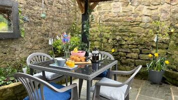 A patio with a stone wall, a table set with breakfast items, and chairs with cushions.