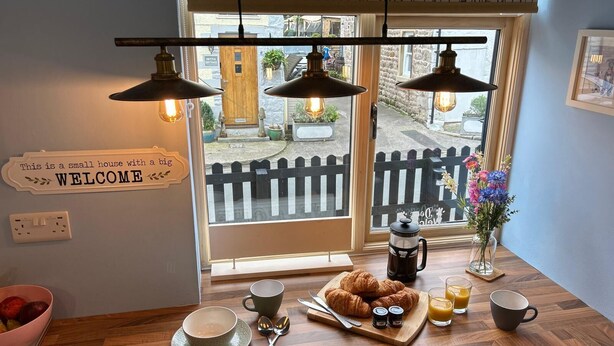 Ontbijt met croissants, koffie en sap op een houten tafel, met een 'WELCOME' bord en uitzicht op een straat.