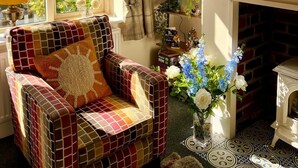 Een gezellige woonkamer met een geruit fauteuil, een open haard en een grote spiegel.