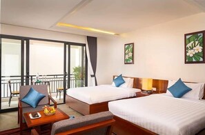 Habitación de hotel con dos camas, balcón, comedor y obras de arte en las paredes.