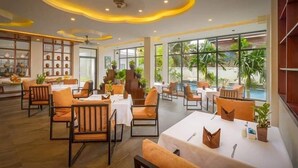 A spacious indoor dining area with multiple tables and chairs, large windows offering views of the outdoors, and a ceiling with recessed lighting. - Angkor Style Resort (Siem Reap)
