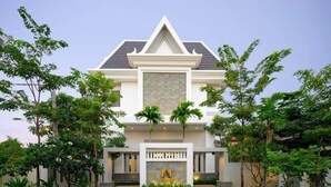 A modern two-story house with a symmetrical facade, a central entrance with a stone facade, and a well-maintained garden with various plants and trees. - Angkor Style Resort (Siem Reap)