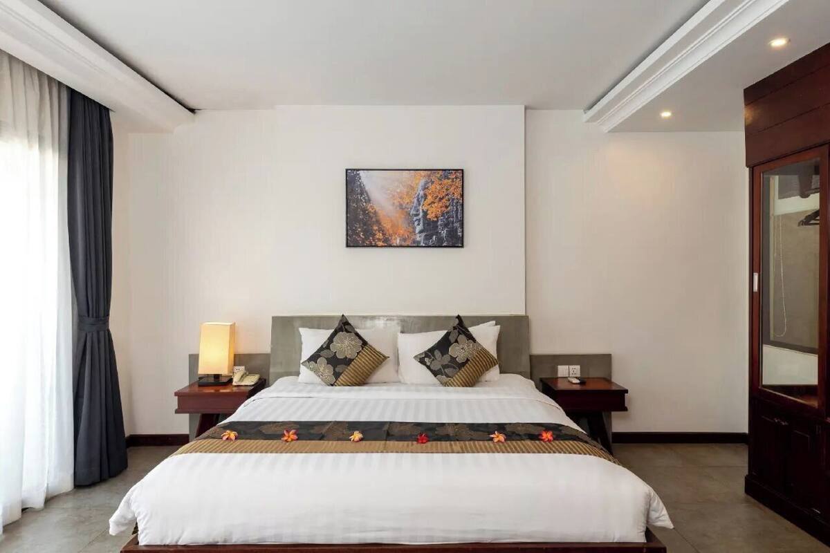 A hotel room with a large bed, a nightstand with a lamp, and a painting on the wall.