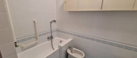 A bathroom with a bathtub, a bidet, and a cabinet.