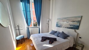 A bedroom with a bed, a chair, a radiator, a painting, and a window with curtains. - Santa in Caruggio- PortofinoVacanze (Santa Margherita Ligure)