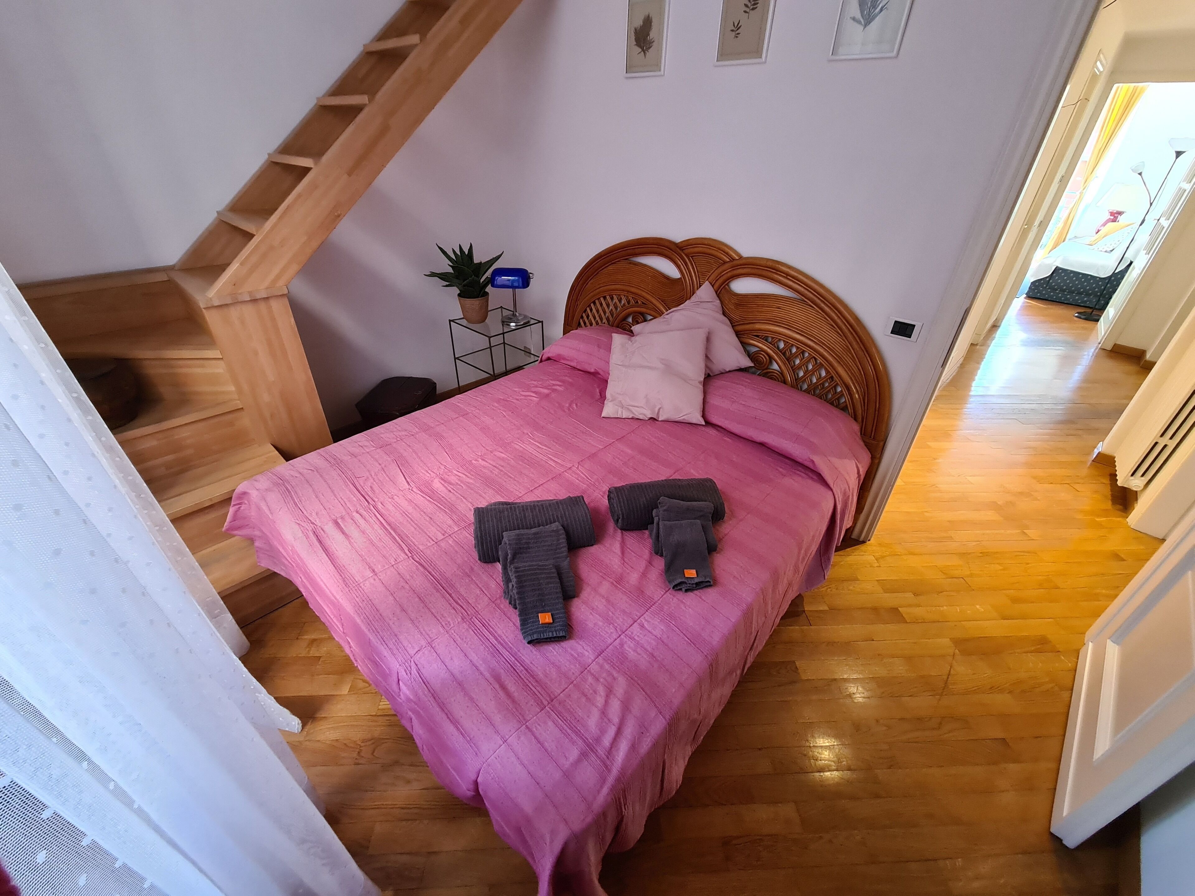 A bedroom with a wooden bed, a pink bedspread, and a wooden staircase.