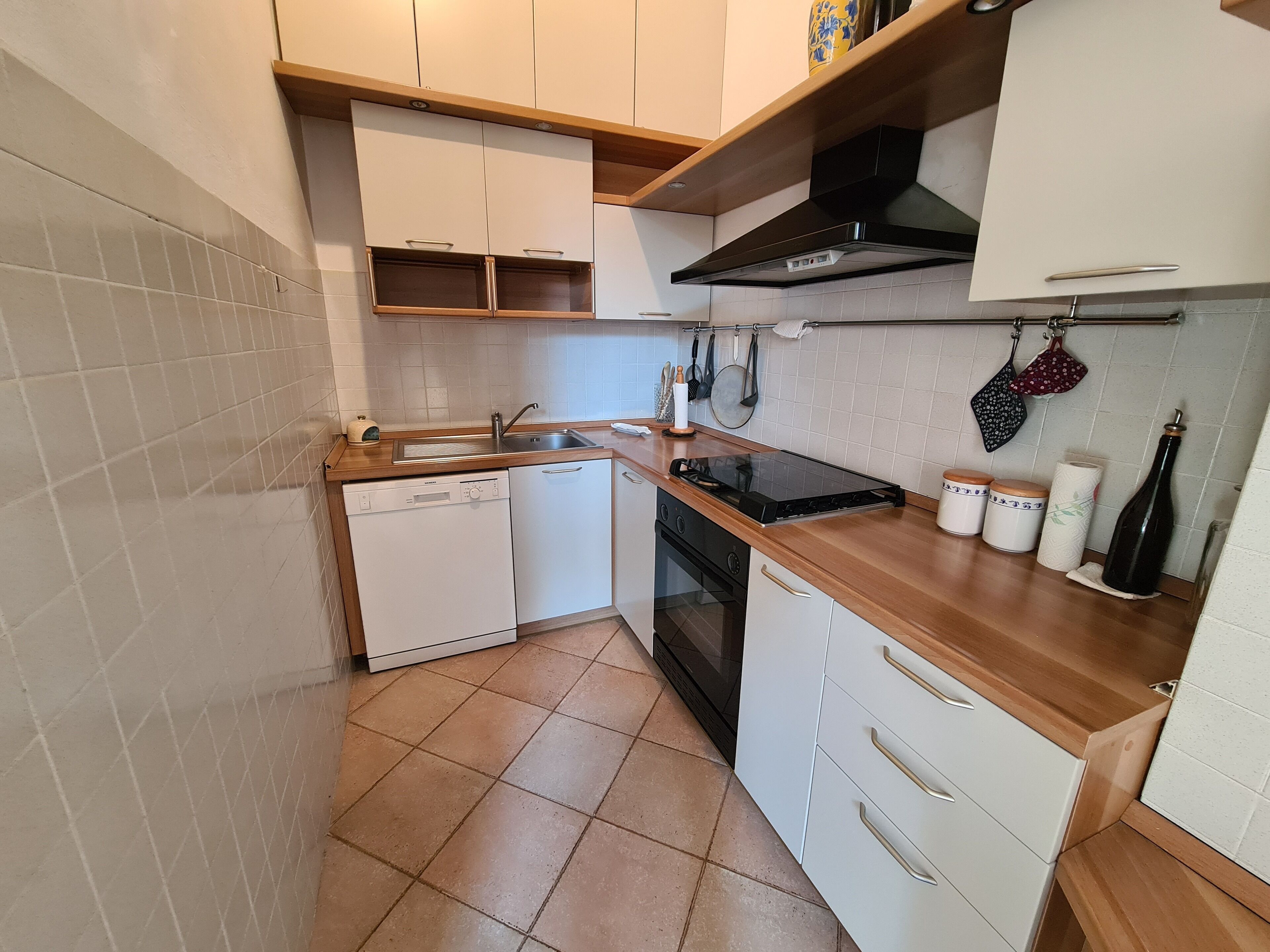 Een compacte keuken met een vaatwasser, fornuis en oven, houten aanrechtblad en witte kastjes.