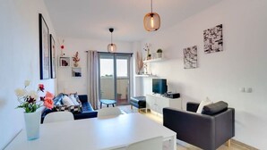 A modern living room with a white dining table, grey sofa, and a TV on a white cabinet. There are framed pictures on the wall and a vase with flowers on the table. - Unique accommodation with a private pool, sea view, terrace, 300m to Aldea Beach (Manilva)