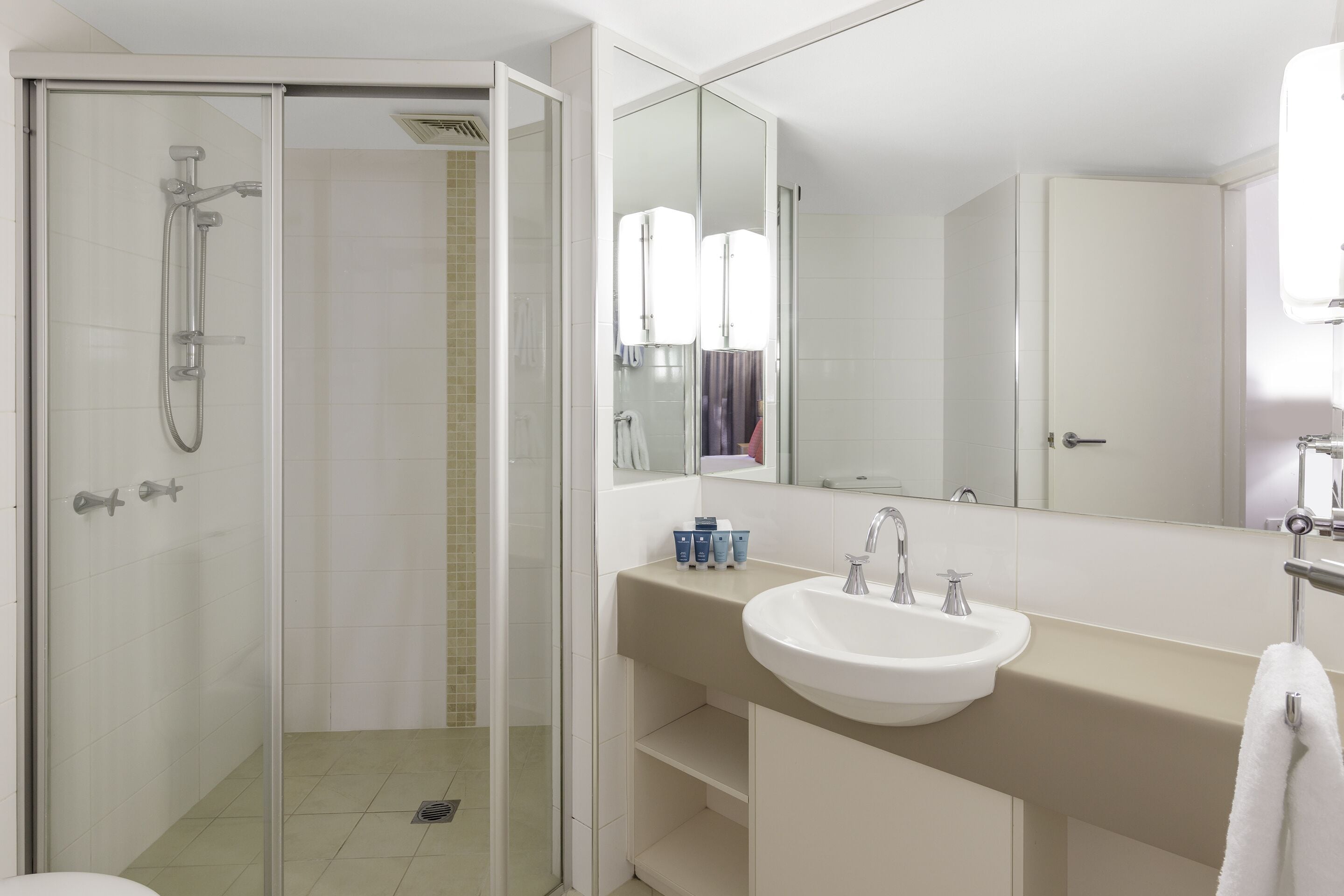Une salle de bain moderne avec une douche à parois de verre, un lavabo blanc et un grand miroir.