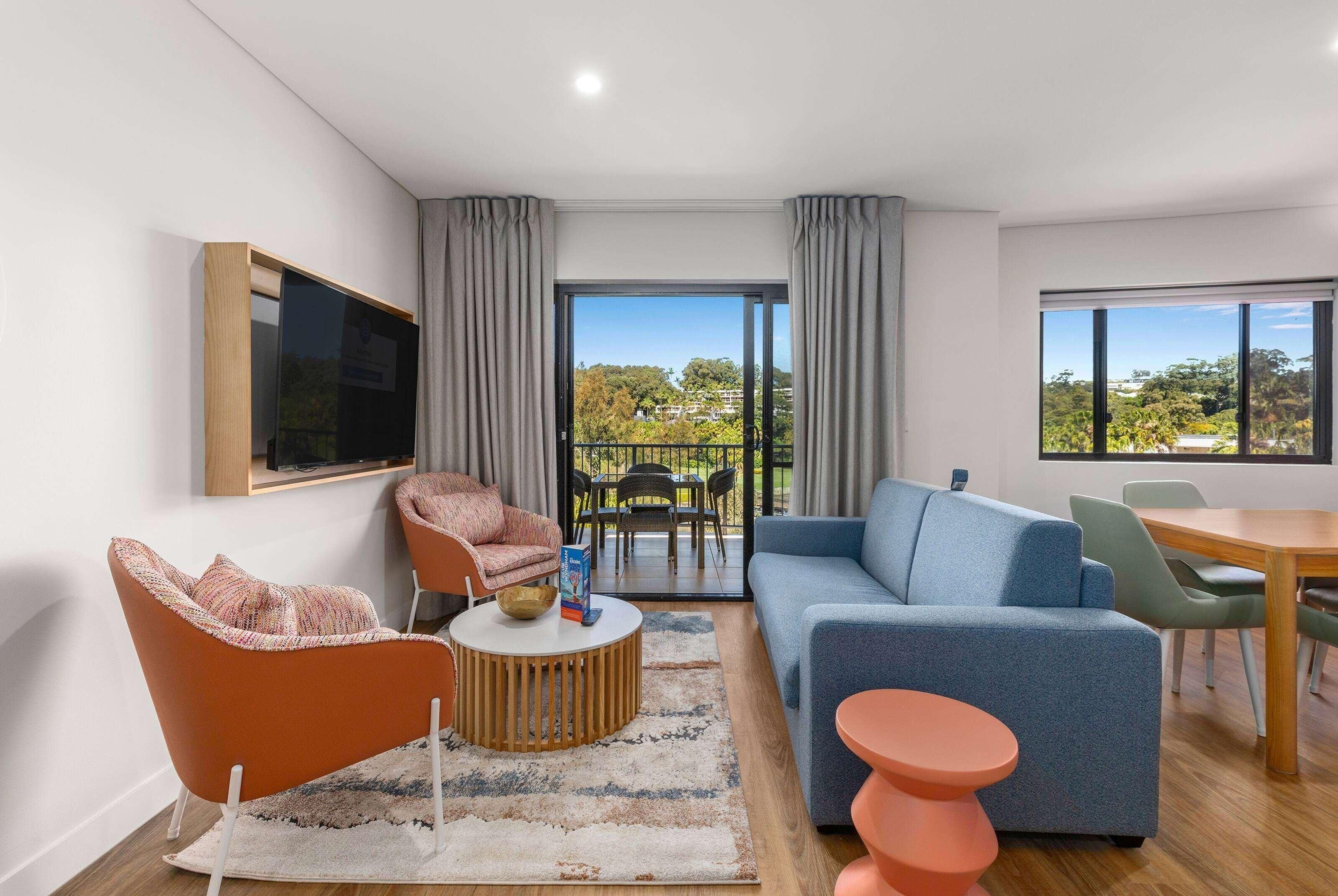 A modern living room with a sofa, armchair, coffee table, and a television mounted on the wall.