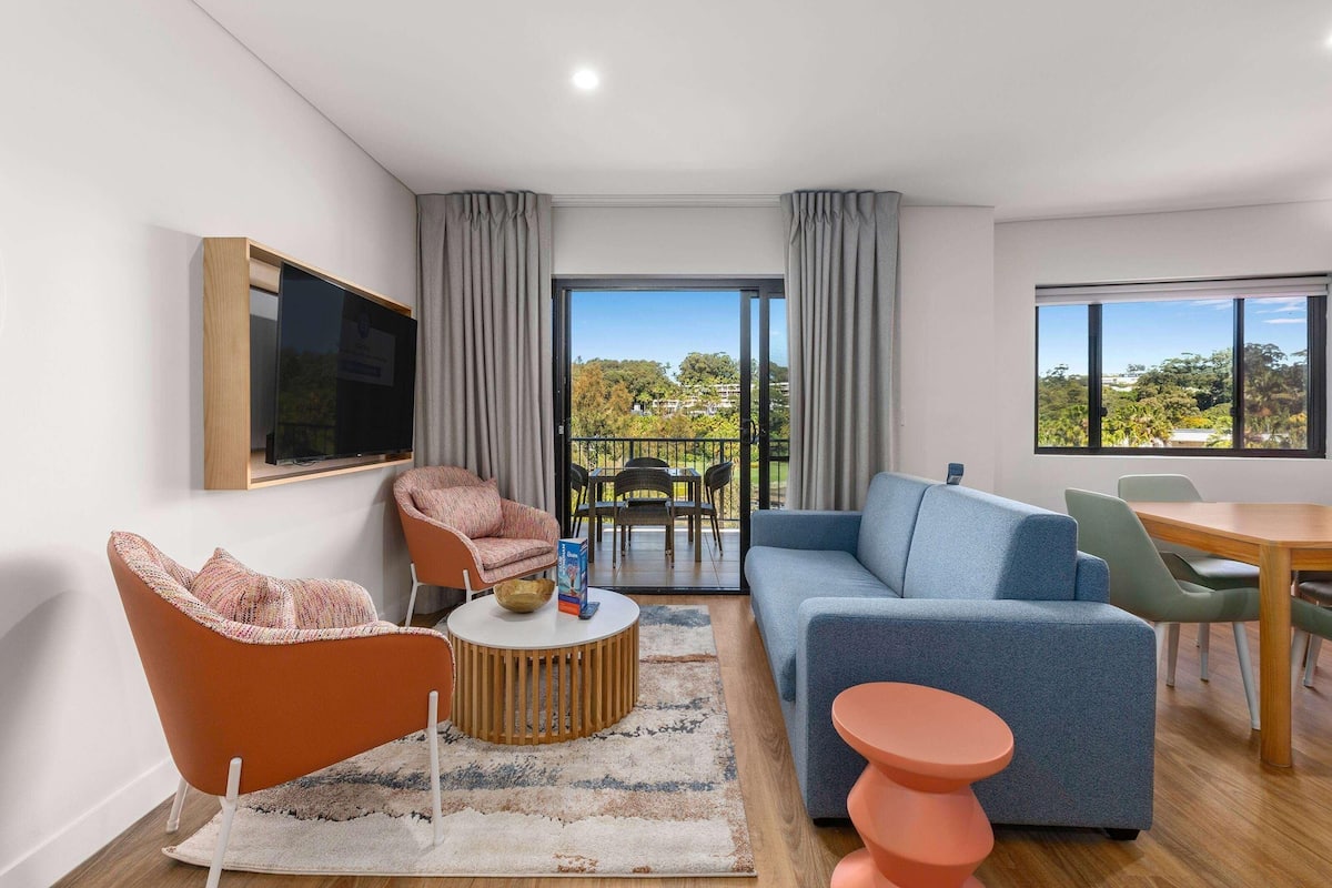 A modern living room with a sofa, armchair, coffee table, and a television mounted on the wall.