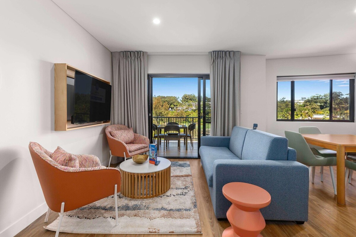 Una sala de estar moderna con sofá, sillón, mesa de centro y televisor montado en la pared.