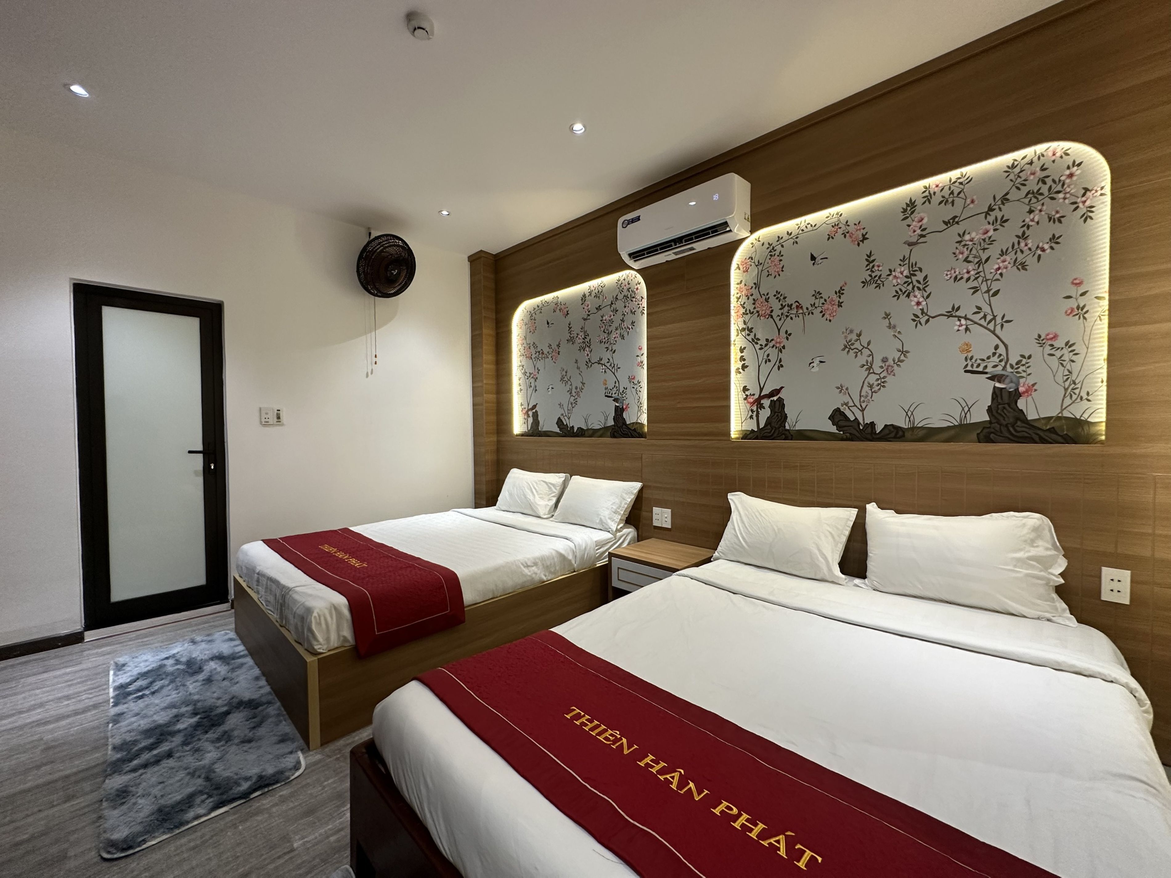 A hotel room with two beds, a wooden headboard, an air conditioning unit, and a wall-mounted air purifier.