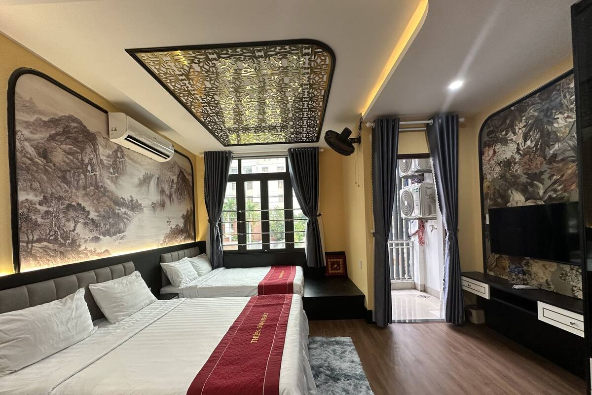 A hotel room with two beds, a large decorative ceiling, a wall-mounted TV, and a balcony with a view.